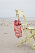 Crocheted beach bag hanging on wooden chair on beach