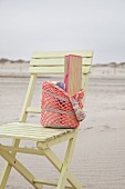 Straw mat in crocheted beach bag on wooden chair on beach