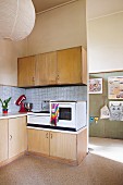 Simple retro kitchen area with electronic appliances on base units and pale wooden wall units