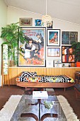Glass-topped coffee table and couch with ethnic blanket against half-height, continuous sideboard below collection of pictures on wall