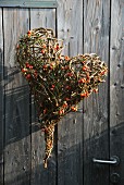 Love-heart formed from twigs and rose hips hung on wooden door