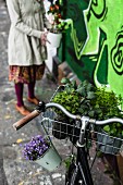Bicycle decorated with plants in front of wall covered in graffiti