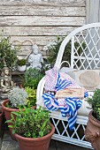 Potted herbs, Buddha statue and white orchids next to white wicker chair in garden