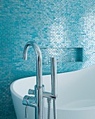 Moderne Standarmatur und Designerbadewanne vor blau schimmernden Mosaikfliesen
