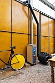 Bicycle and locker on castors next to black Bullerjan stove in front of tall wood and metal wall