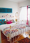 White metal bed in bright bedroom with various accents of bright colour
