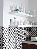 Fliesen mit schwarz-weißem, geometrischem Muster an Wand, oberhalb Regalböden mit Geschirr und Dekofiguren in Weiß