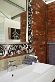 Mirror with ornate, floral silver frame and trough-style sink on brick wall