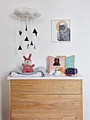 Mobile of black triangles hanging from cushioned cloud above changing unit with plain wood drawers and white worksurface