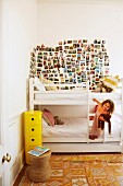 Little girl climbing on ladder of white bunk beds below large collection of postcards on wall