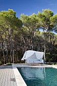 Pool and elegant white couch with white canopy as windbreak in front of pine woods