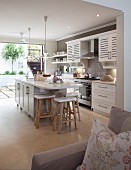 View past sofa into country-house kitchen with breakfast bar and bar stools