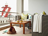 Floral scatter cushions on wicker sofa and coffee table on balcony with view of red and white lighthouse