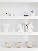 Decorative white vessels and china horses heads on white shelves