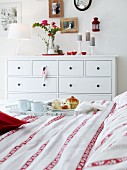 A breakfast tray and a red and white patterned duvet with a simple, country house-style white chest of drawers in the background