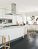 White designer kitchen with bar stools at counter and plants hanging in window