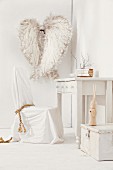 Chair with white loose cover at rustic writing desk; decorative angels wings on wall in background