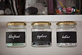 Labelled storage jars with lids attached to bottom of shelf by magnets