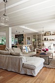 Offener Wohnbereich in Landhausstil mit gemütlicher beigefarbener Polstercouch und weißer Holzbalkendecke