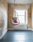 Hanging chair with cushions in front of window in room with patinated walls