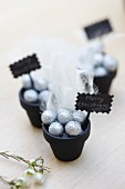 Plant pots painted black and decorated with baubles and feathers as festive table ornaments