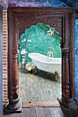 Blick durch Türöffnung mit geschnitztem Holzrahmen auf freistehende Vintage Badewanne vor grüner Wand