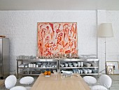 Crockery on stainless steel shelves below modern artwork on whitewashed brick wall