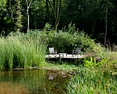 Idyllic seating area on sunny wooden deck next to pond