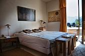 Schlafzimmer im Ethnostil, drei Holzhocker als Ablage am Fußende, Blick durch offene Terrassentür