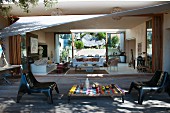 Terrasse mit Sonnensegel, buntem Tischchen und modernen Stühlen aus Kunststoff, Blick in den Wohnraum