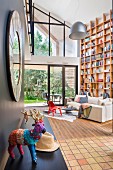 Animal ornament covered in colourful yarn on black shelf and sofa in front of floor-to-ceiling bookcase in contemporary living room