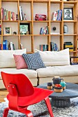 Red, classic chair and rustic coffee table in front of pale sofa and wooden shelving against wall in modern living room
