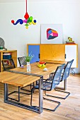 Dining table with wooden top mounted on metal frame, metal cantilever chairs, postmodern pendant lamp and sideboard with colourful doors in background
