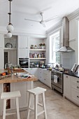 Modern country-house kitchen with white cupboards and free-standing central counter with white-painted bar stools