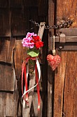 Walking stick decorated with geraniums next to small fabric heart hung on wooden door