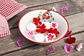 Geranium flowers and candles floating in vintage enamel bowl on wooden table