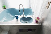 Small, colourful figurines on organically shaped, pale blue sinks recessed in monolithic washstand with silver-painted surface