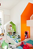 Custom-made house-shaped canopies over children's beds with interiors painted in bright colours; toddler playing on bed