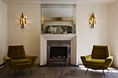 Objets d'art on mantelpiece of fireplace with postmodern surround flanked by hand-crafted sconce lamps and two retro armchairs