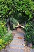 Garden patch made from old railway sleepers leading to table & chairs in secluded seating area in garden below trees