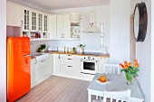 White, open-plan fitted kitchen with orange retro fridge and small dining area