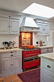 Country-house-style, fitted kitchen painted pale grey with red gas cooker under extractor hood and skylight