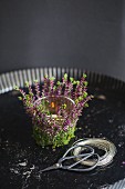 Tealight holder wrapped in springs of heather next to wire and shears in quiche tin