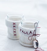 White knitted teacup cosies embroidered with pattern of crosses and name
