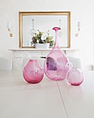 Round, pink glass vases on table in front of mirror above fireplace