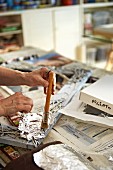 Hands of person applying silver leaf to picture frame in artist's studio