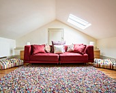 Many scatter cushions on red couch and multicoloured rug in attic room with skylight