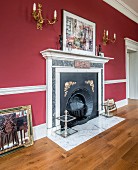 Elegant fireplace with mantelpiece below gilt sconce lamps on red wall in grand room
