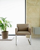 Modern cantilever chair with beige leather cover and metal legs in front of large window in stone wall