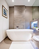 Moderne freistehende Badewanne vor einer Natursteinwand mit beleuchteter Nische
